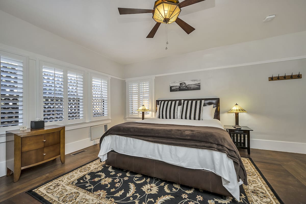 A bedroom with a large bed, a ceiling fan, a nightstand with a lamp, and a wooden dresser.