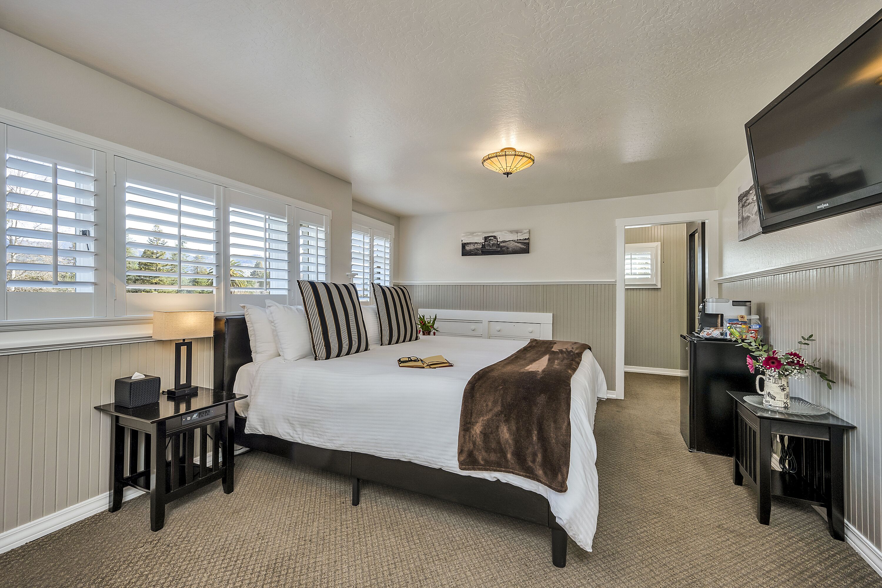 A bedroom with a bed, bedside tables, a lamp, a TV, and a window with blinds.
