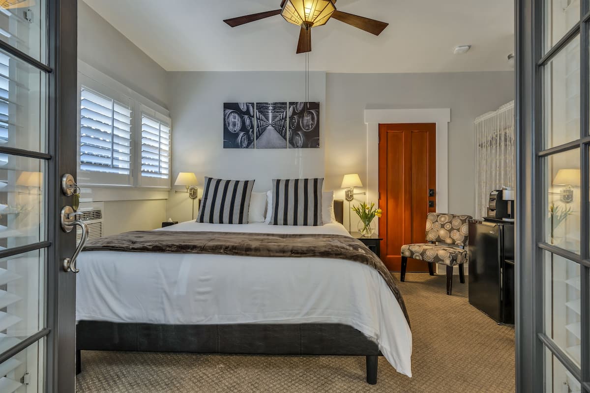 A bedroom with a bed, a chair, a desk, a ceiling fan, and a door.