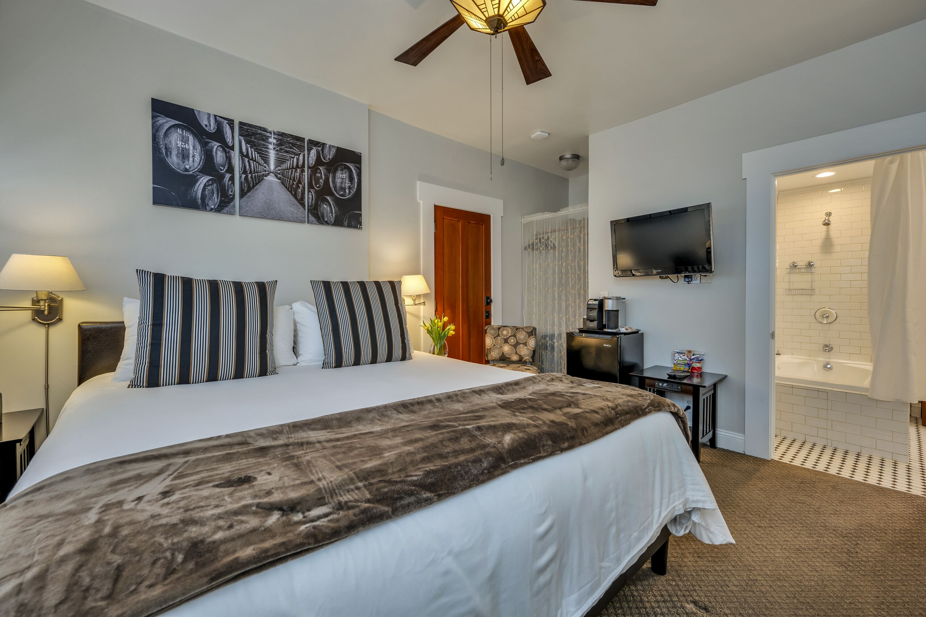 Ein Hotelzimmer mit einem großen Bett, einem Fernseher, einem Deckenventilator, einer Dusche und einer Tür zu einem anderen Raum.