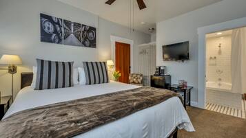 Ein Hotelzimmer mit einem großen Bett, einem Fernseher, einem Deckenventilator, einer Dusche und einer Tür zu einem anderen Raum.