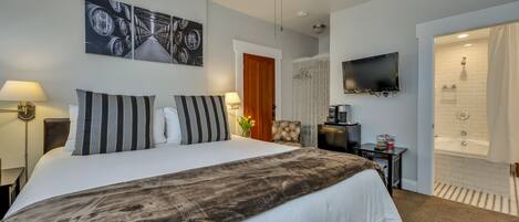 A hotel room with a large bed, a television, a ceiling fan, a shower, and a door leading to another room.