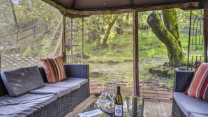 An outdoor seating area with wicker furniture, a glass table, and a bottle of wine.