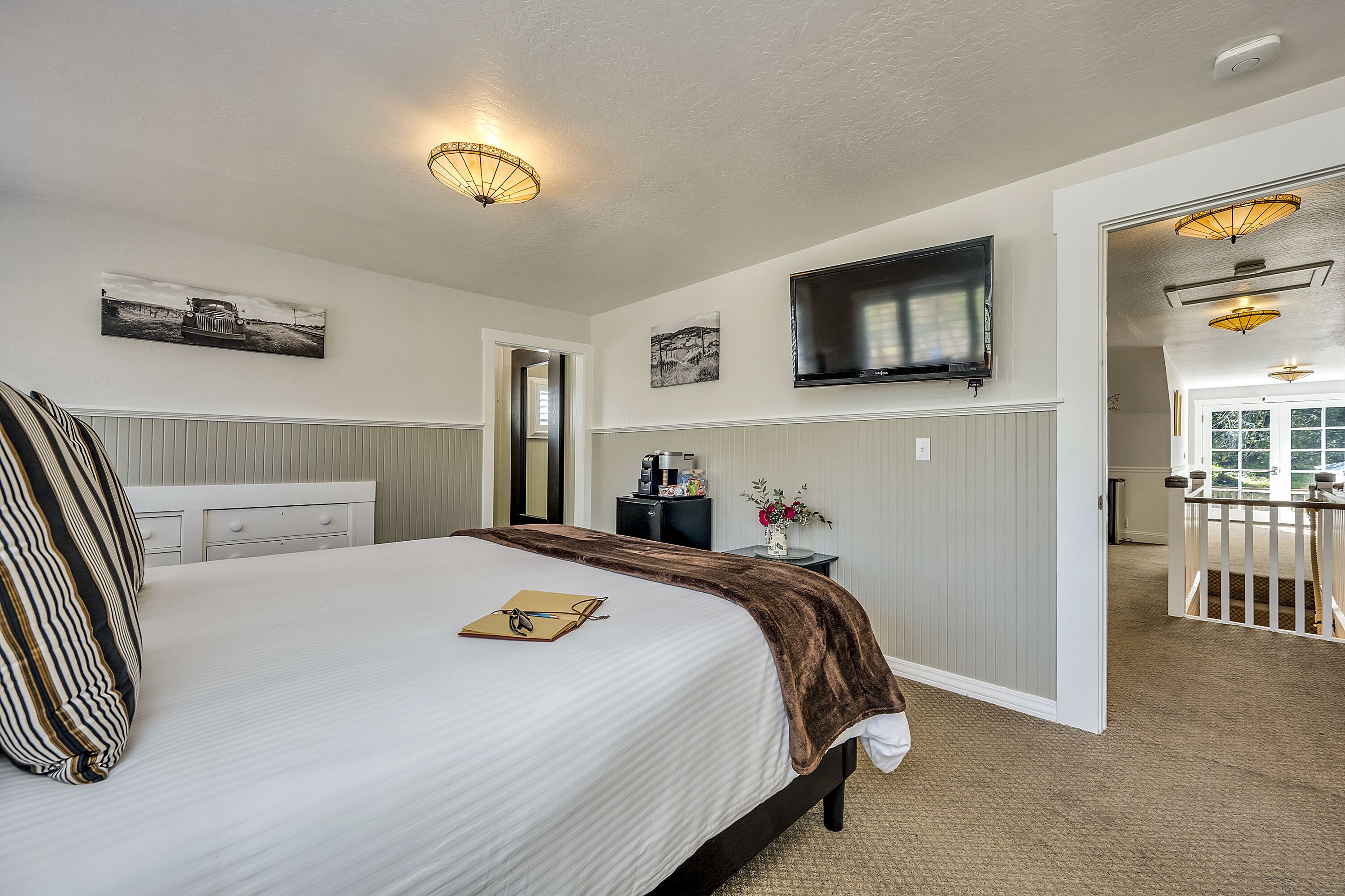Habitación de hotel con una cama grande, un televisor de pantalla plana en la pared, un escritorio con cafetera y vistas al balcón exterior.
