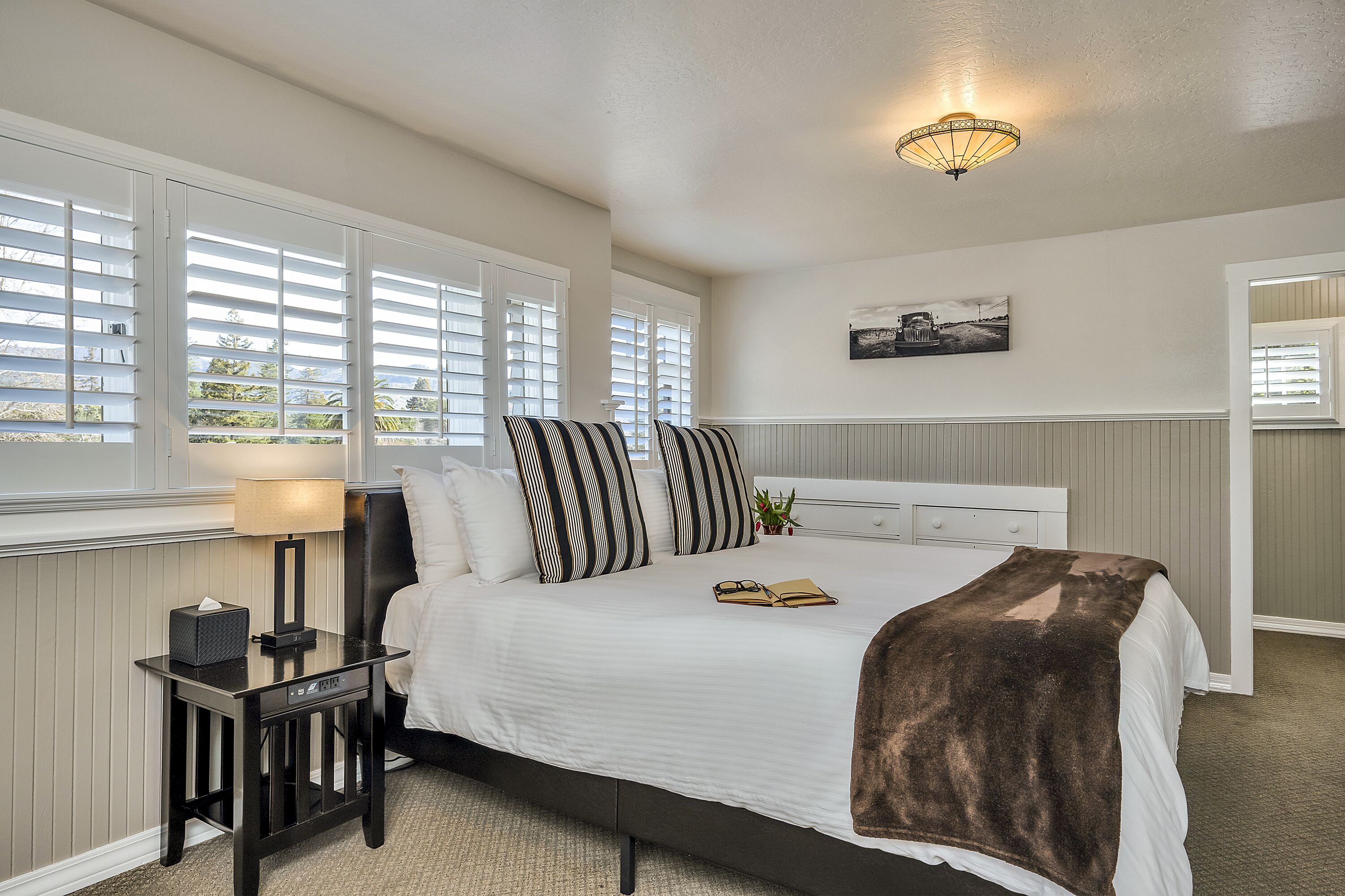 A neatly arranged bedroom with a bed, bedside table, lamp, and a wall-mounted picture.