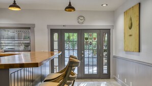 A kitchen with a wooden bar and chairs, a clock on the wall, and a door leading outside.