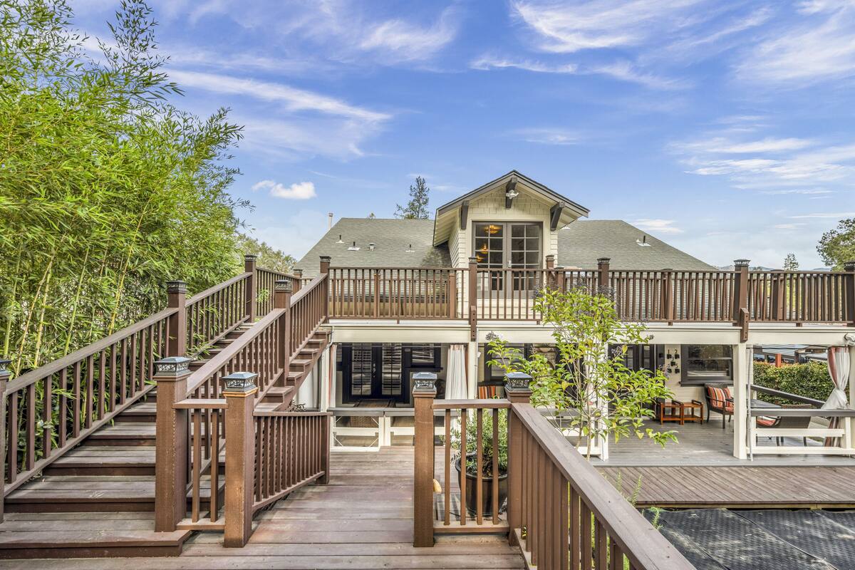 A two-story house with a wooden deck, a covered patio, and a large window.