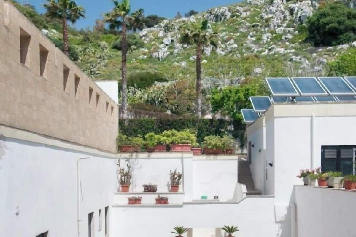 Un patio estrecho con escaleras, paredes blancas, plantas en macetas y paneles solares en el techo.