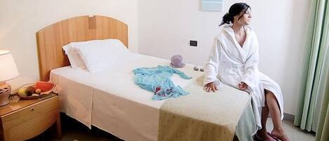 Una habitación de hotel con una cama de madera, una mesita de noche con lámpara y una ventana con cortinas.