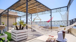 Una terraza en la azotea con una hamaca, asientos al aire libre, una mesa con bebidas y vistas al mar.