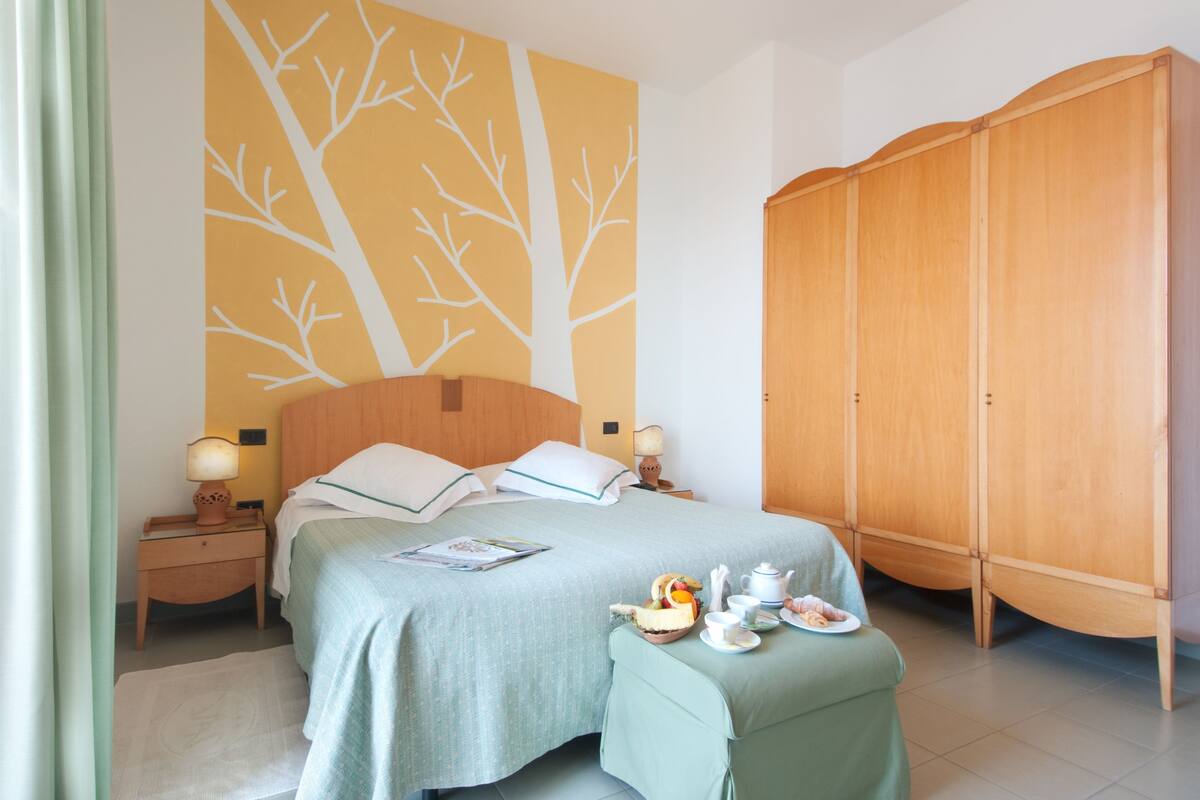 Un dormitorio ordenado con cama, mesitas de noche, armario y un mural en la pared.