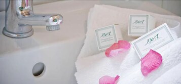 A white bathroom sink with a silver faucet, a white towel, and pink bath products.
