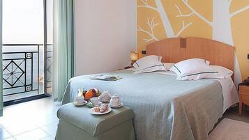 A hotel room with a bed, a nightstand, a table with breakfast items, and a balcony with a railing.