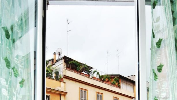 Vista de calle con un edificio de fachada amarilla, un coche rojo estacionado frente a él y un paso de peatones.