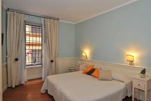 Un dormitorio con una cama, dos mesitas de noche, una ventana con cortinas y lámparas fijadas a la pared.