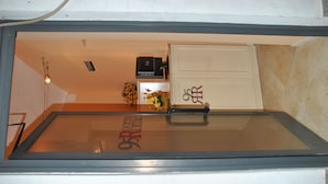 Una habitación con un separador de vidrio, un termostato, una mesita con un jarrón de flores y un armario con cerradura.