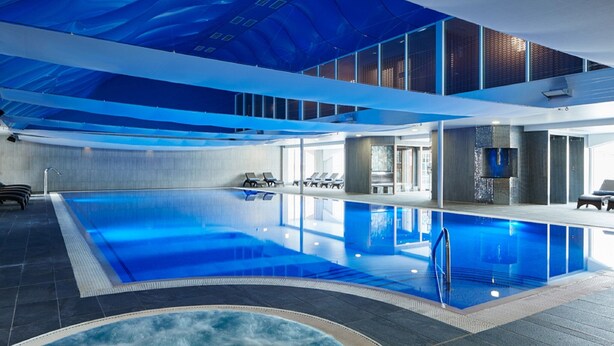 A large indoor swimming pool with clear blue water, a lounge area with chairs, and a modern ceiling design. - Formby Hall Golf Resort & Spa (Liverpool)