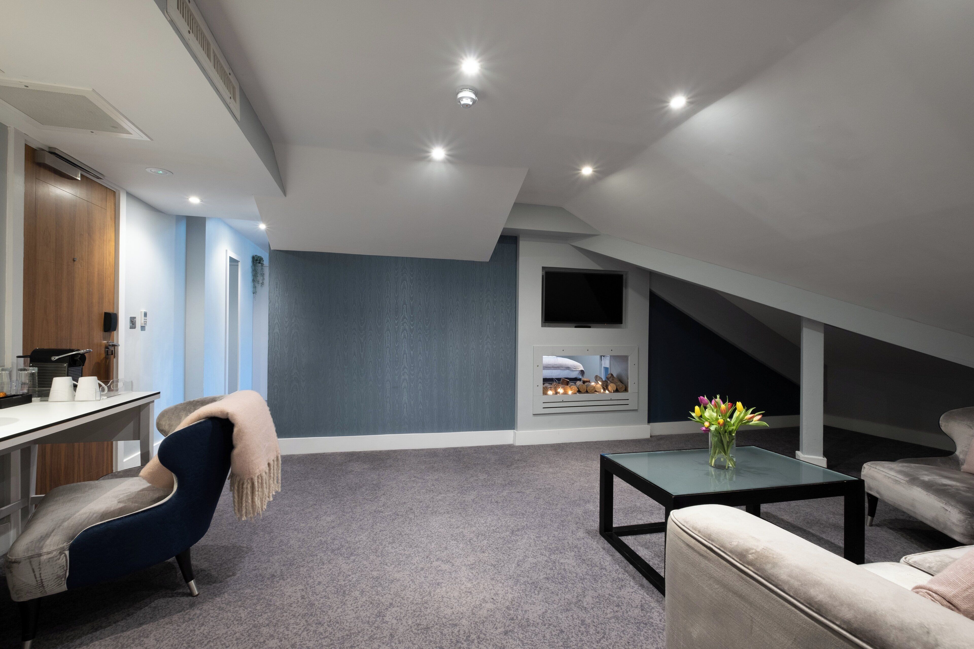 A modern loft-style room with a sloped ceiling, a built-in fireplace, and a seating area with a sofa and armchair.