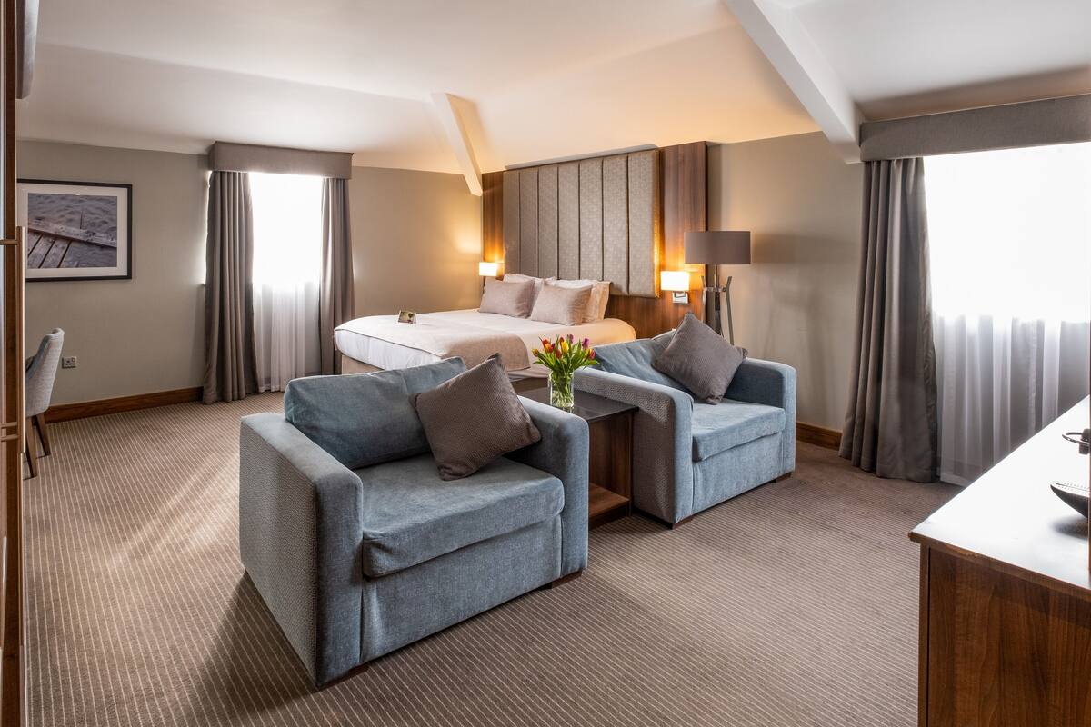Ein Hotelzimmer mit einem Bett, zwei Sesseln, einem kleinen Tisch und einem Schreibtisch.