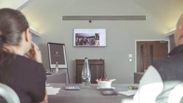 A conference room with a large screen displaying a presentation, a projector, a water bottle, a small vase, and a white mug on the table.
