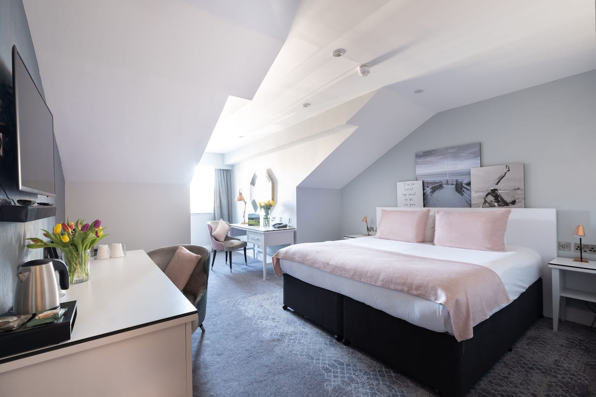 Ein modernes Hotelzimmer mit einem großen Bett, einem Schreibtisch, einem Sessel und einem Fernseher.