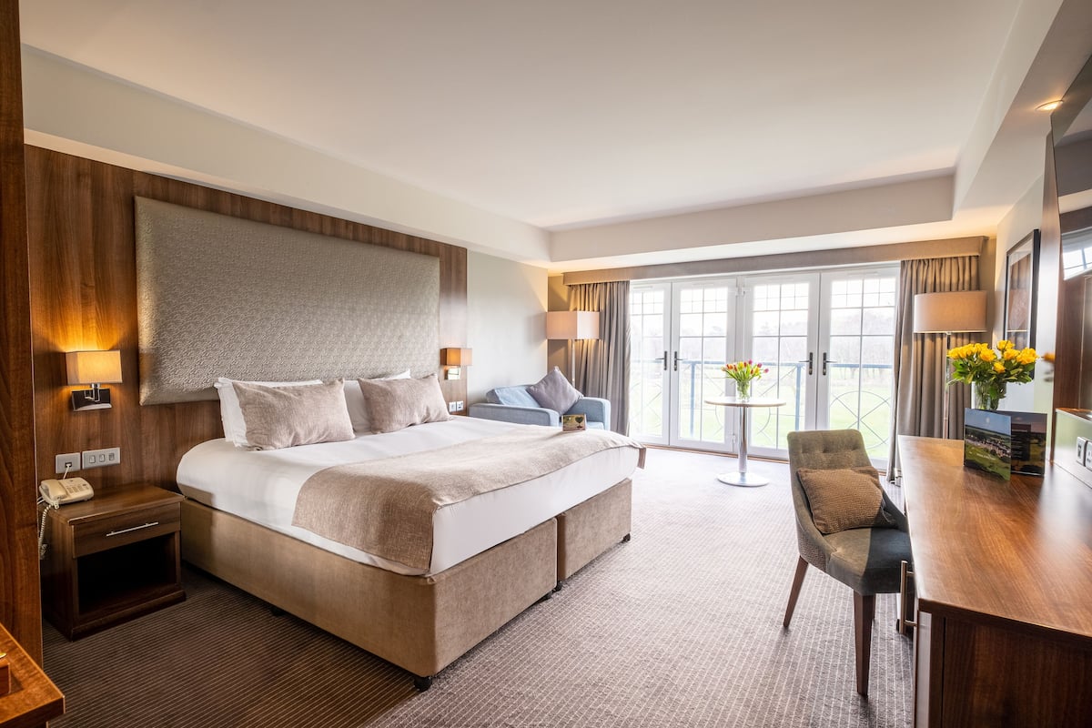 Ein Hotelzimmer mit einem großen Bett, einem Schreibtisch, einem Sessel und einem Balkon mit Aussicht.