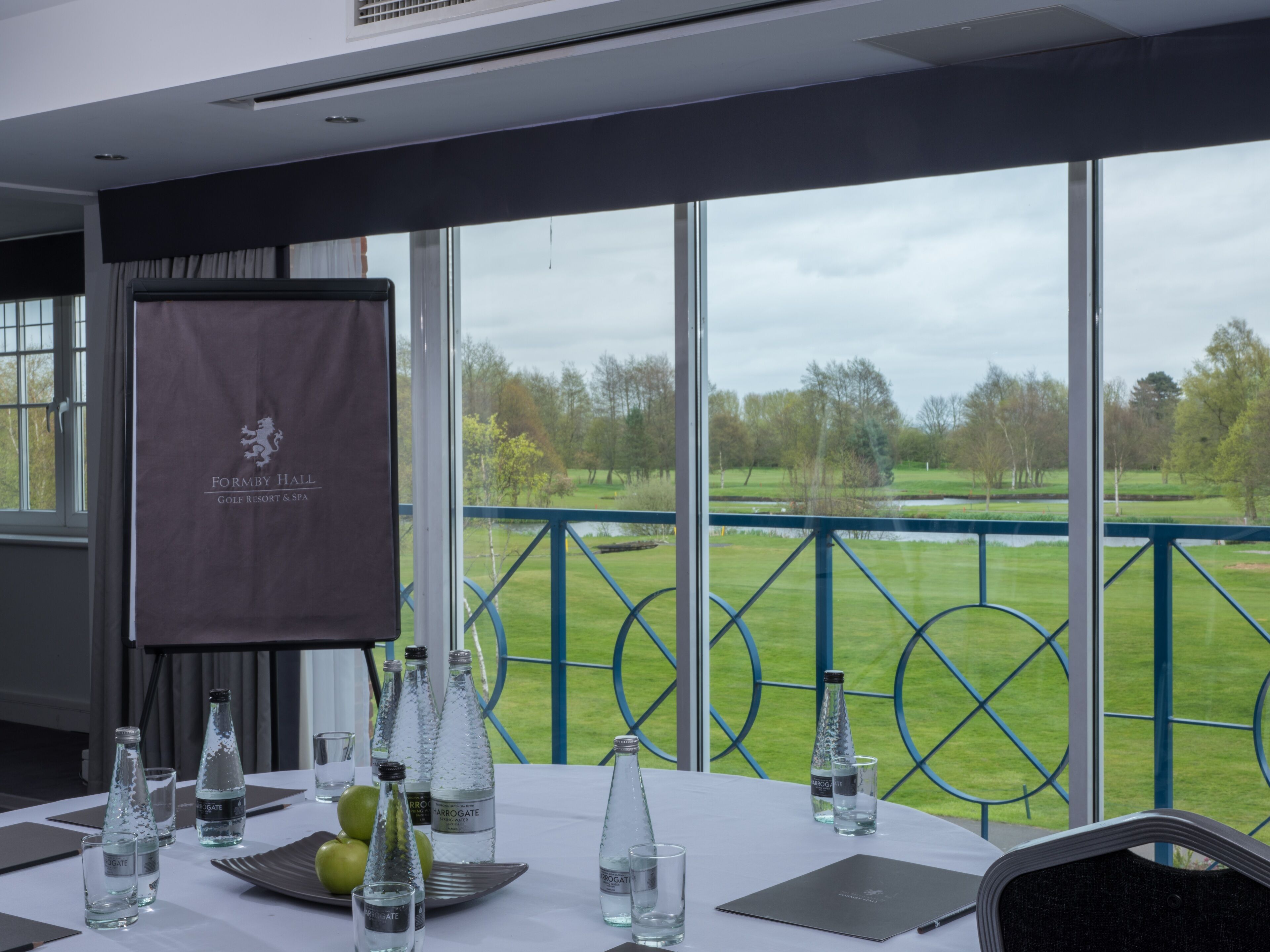 A conference room with a view of a golf course, a banner with the hotel name, and water bottles on the table.