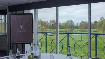 A conference room with a view of a golf course, a banner with the hotel name, and water bottles on the table.