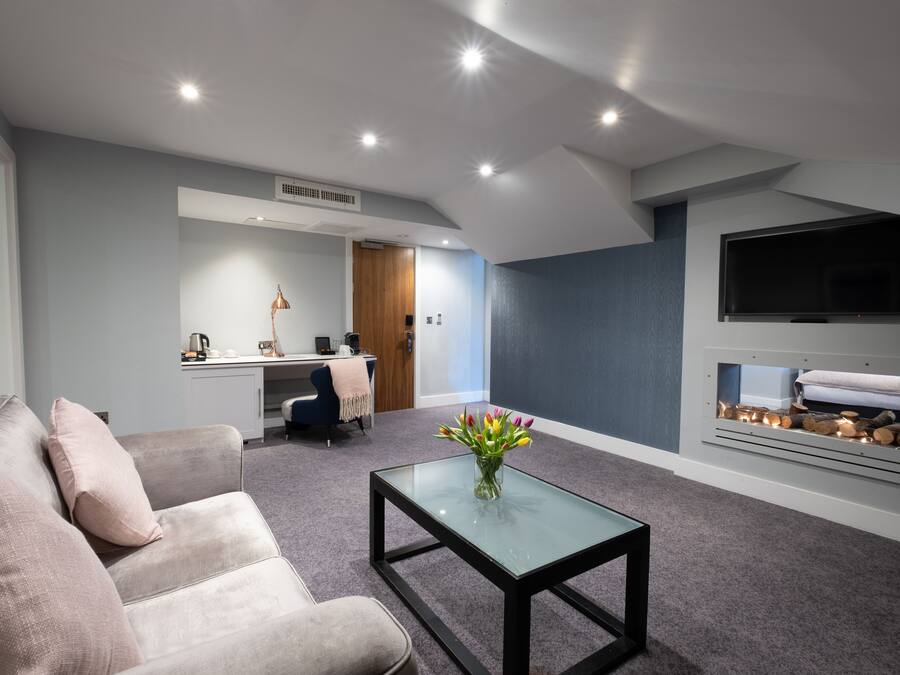 A modern living room with a sofa, a glass coffee table, a TV mounted on the wall, and a fireplace.