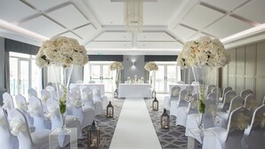A wedding venue with white chairs, a white aisle, and floral centerpieces. - Formby Hall Golf Resort & Spa (Liverpool)