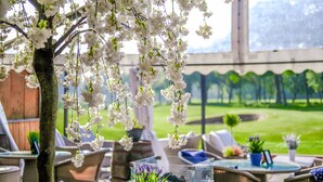 An outdoor seating area with wicker furniture, a small tree with white flowers, and a view of a green lawn. - Formby Hall Golf Resort & Spa (Liverpool)