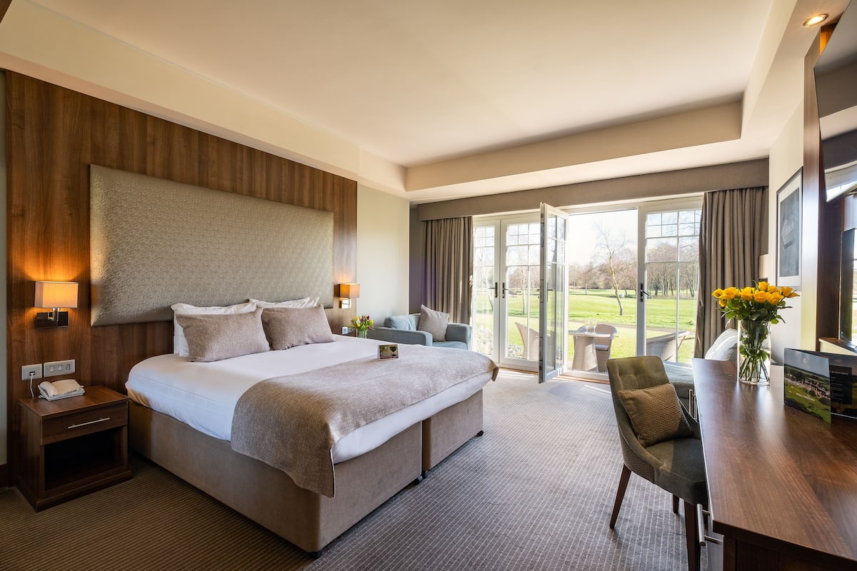 Ein modernes Hotelzimmer mit einem großen Bett, einem Schreibtisch, einem Stuhl und Blick ins Freie.