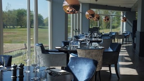 A restaurant with large windows, round tables, and blue chairs. - Formby Hall Golf Resort & Spa (Liverpool)