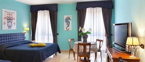 A hotel room with a large bed, a desk with a TV, a dining table, and two chairs.