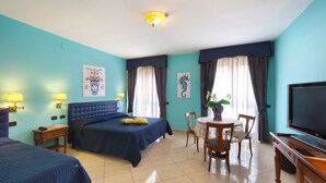 Habitación de hotel con dos camas, una mesa de comedor, sillas, televisor y obras de arte en las paredes.