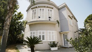 Un edificio de dos pisos con un balcón curvo, contraventanas blancas y un porche con una puerta.