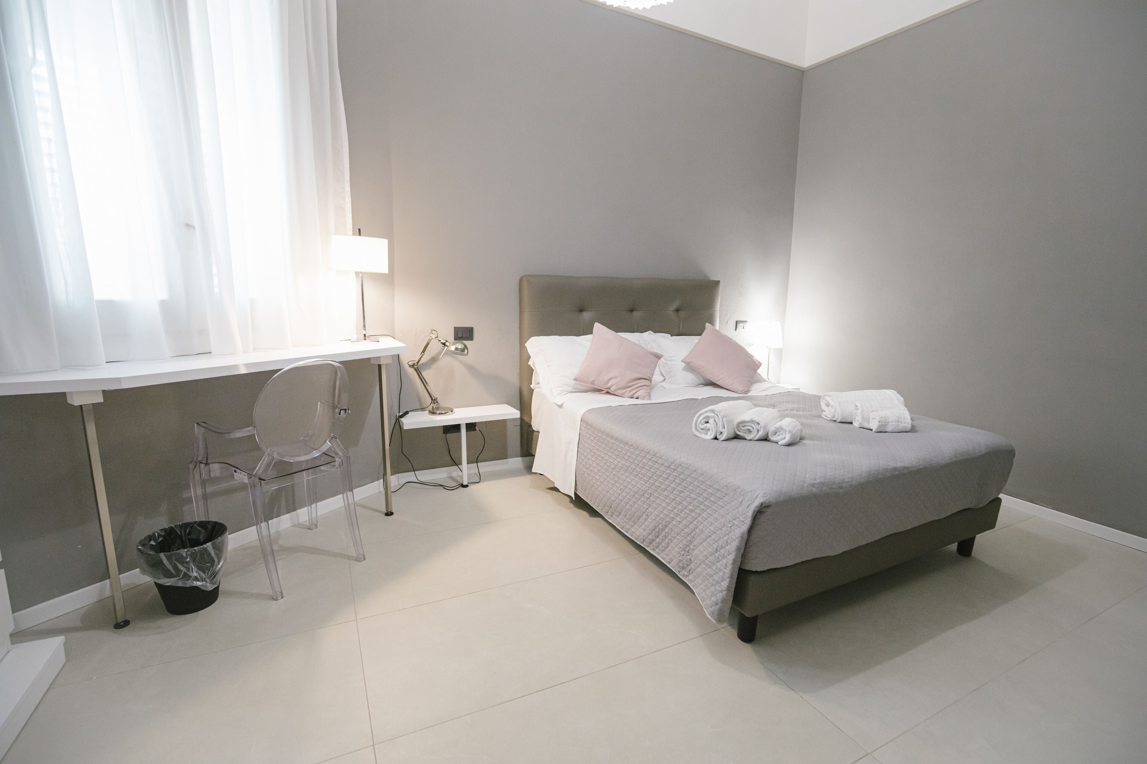 Ein Schlafzimmer mit Bett, Nachttisch, Lampe, Stuhl und Mülleimer.