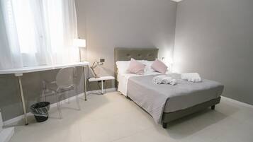 Ein Schlafzimmer mit Bett, Nachttisch, Lampe, Stuhl und Mülleimer.