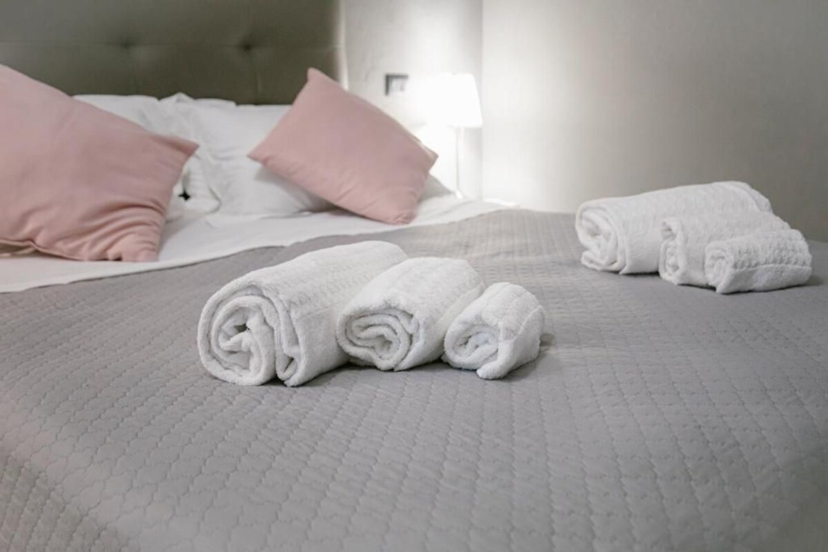 A neatly made bed with rolled white towels and pink pillows.