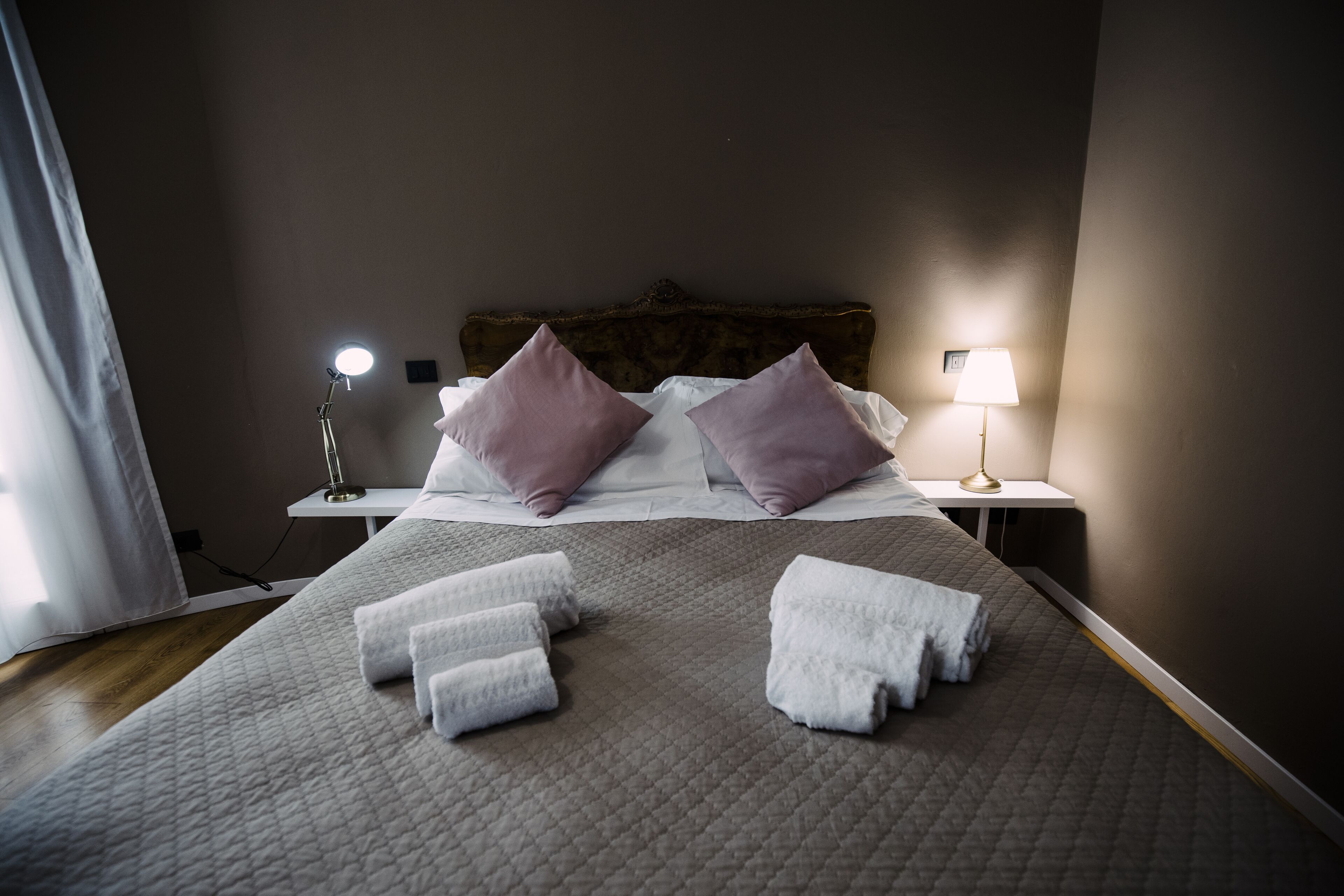 A neatly made bed with pillows, two bedside lamps, and folded towels on a bed with a quilted cover.