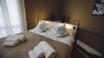 A neatly made bed with white linens and decorative pillows, a bedside table with a lamp, and a painting on the wall.