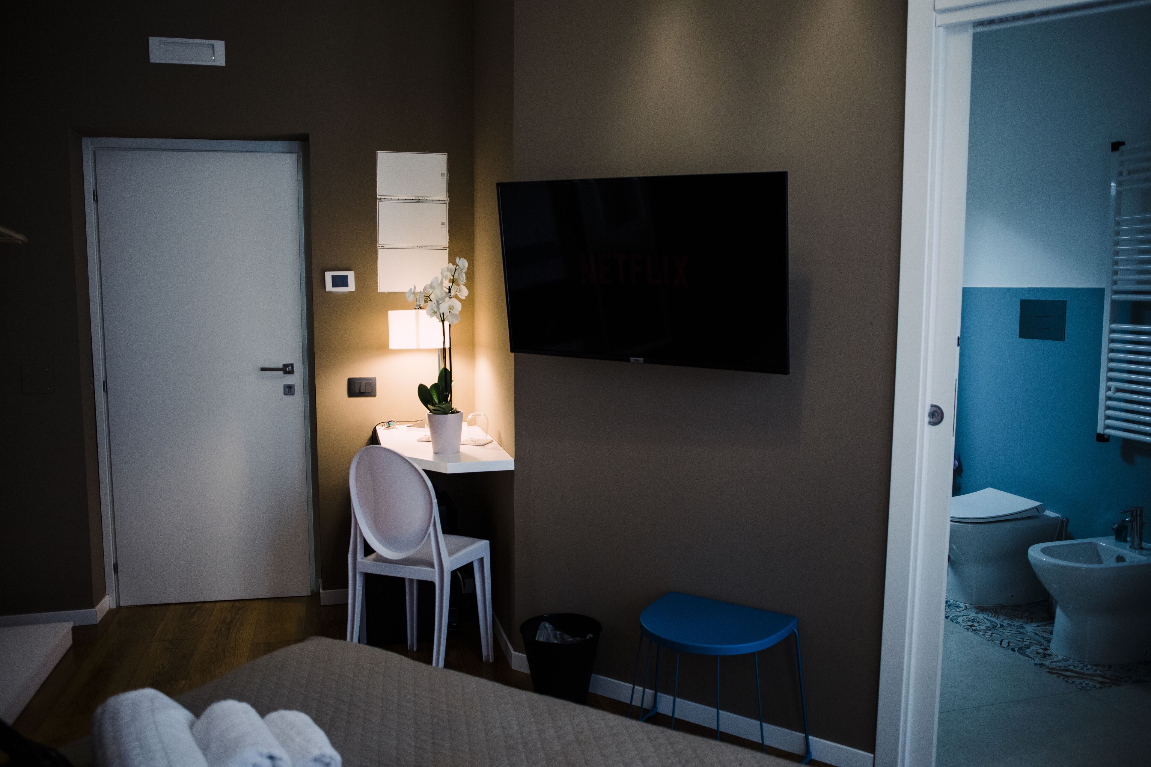 A hotel room with a bed, a desk with a chair, a TV, and a bathroom visible through an open door.