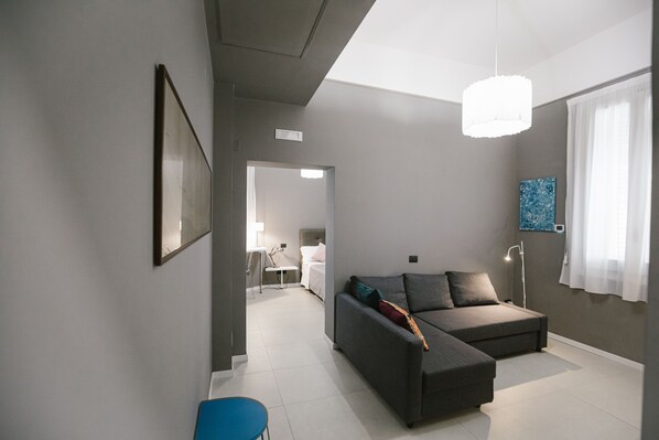A modern living room with a grey sofa, a blue chair, and a large window with white curtains.