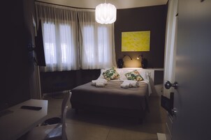 Una habitación de hotel con cama, escritorio, silla, televisor y un ventanal con cortinas.