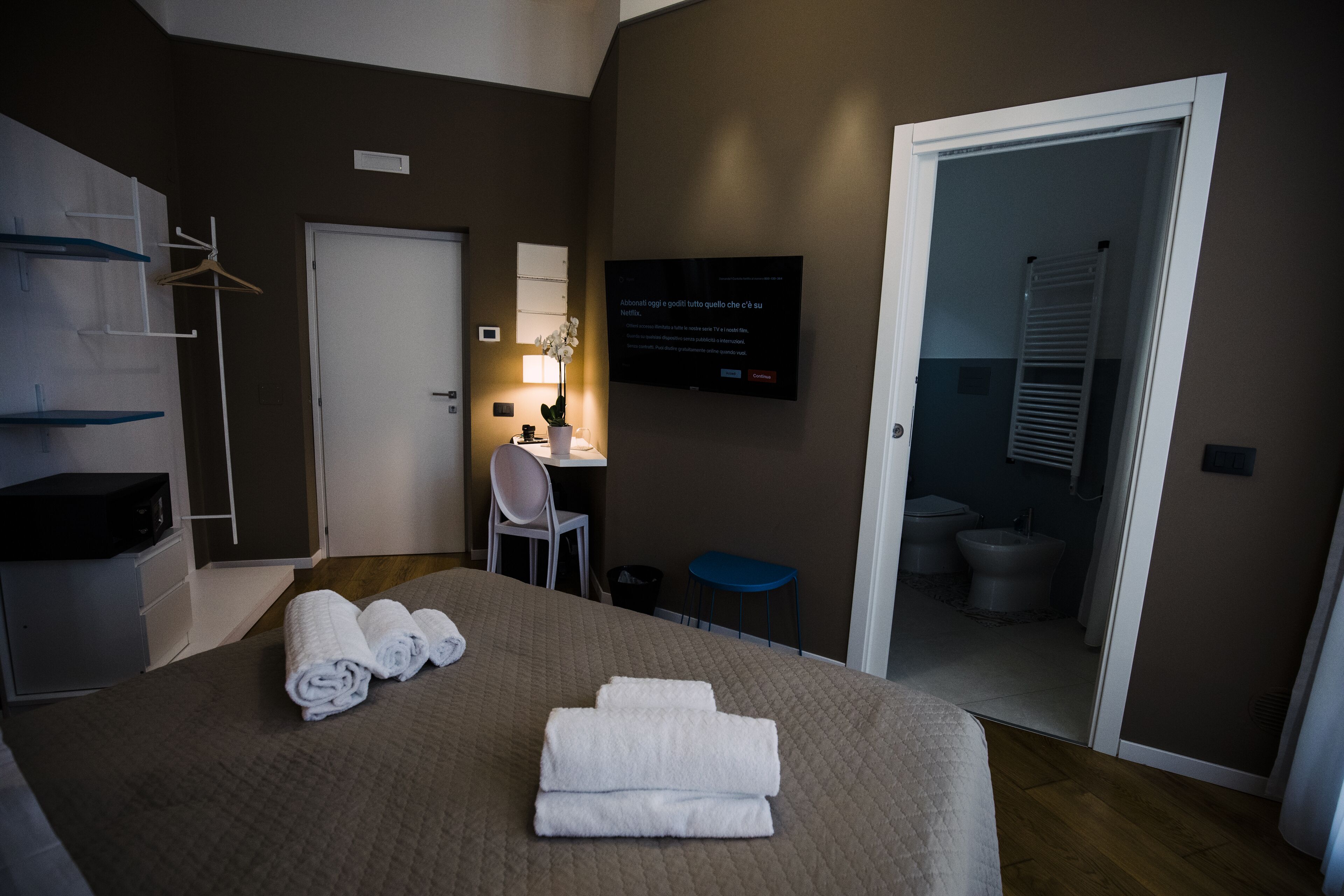 A hotel room with a bed, a desk, a chair, a TV, and a bathroom visible through an open door.