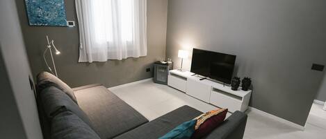 Una sala de estar moderna con un sofá gris, un televisor de pantalla plana, una mesita auxiliar y un armario blanco.