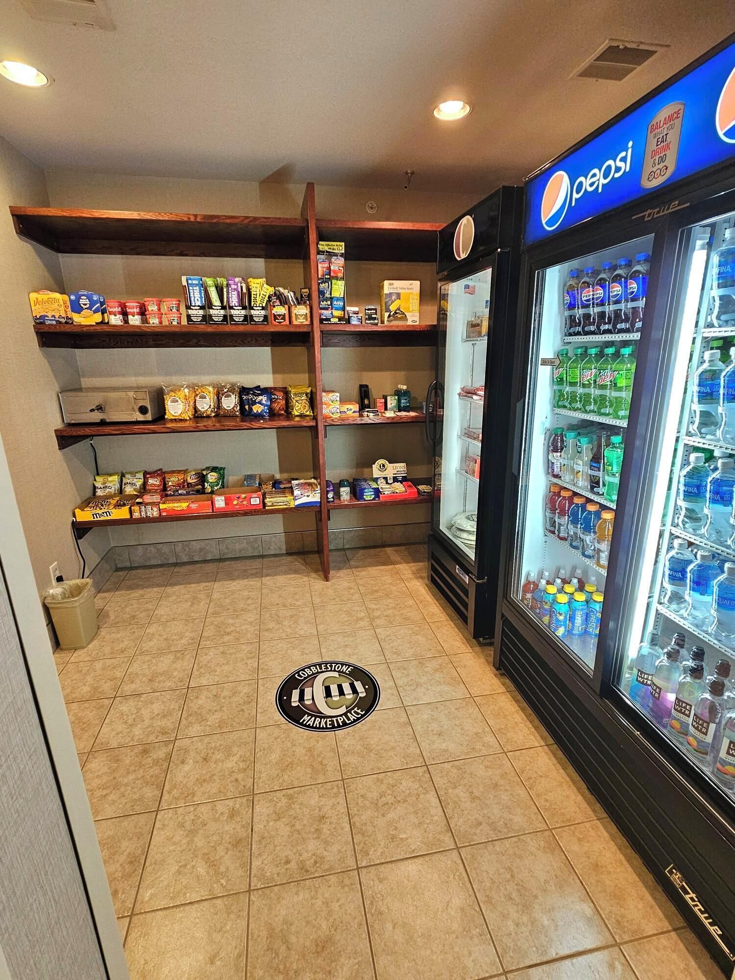 Zona de máquinas expendedoras con Pepsi y Mountain Dew, estantes llenos de snacks y bebidas, y el logotipo de Cobblestone Marketplace en el suelo.