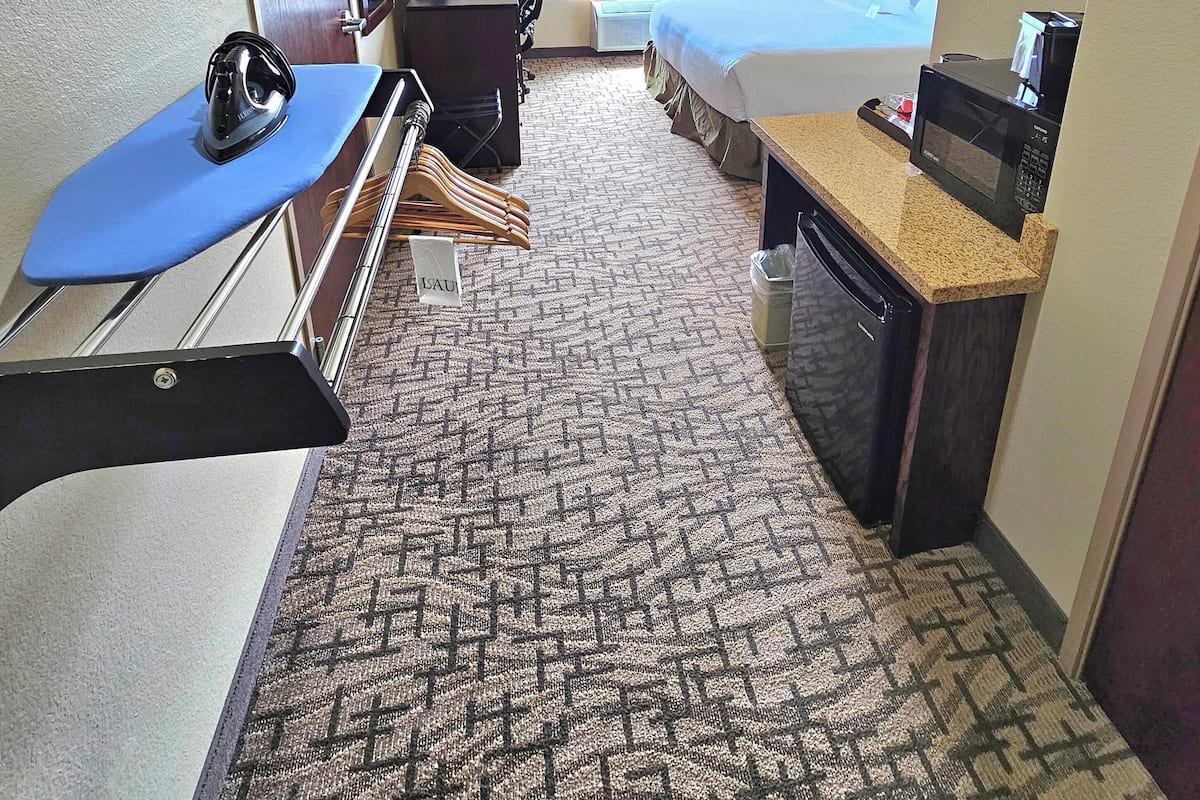 A hotel room with a bed, a desk with a computer, a microwave, and a small kitchenette.