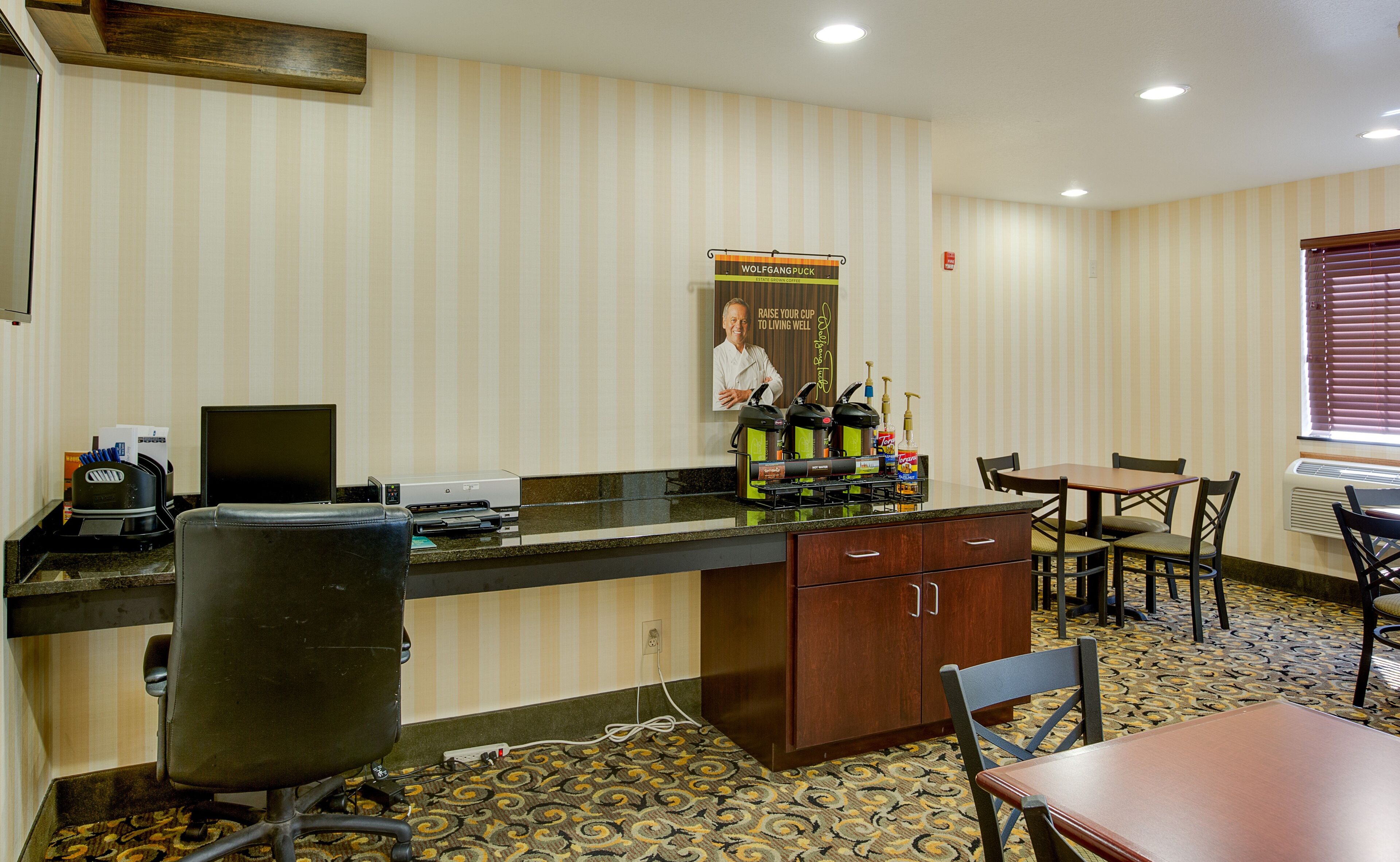 A hotel room with a kitchenette, a dining area, and a poster on the wall.