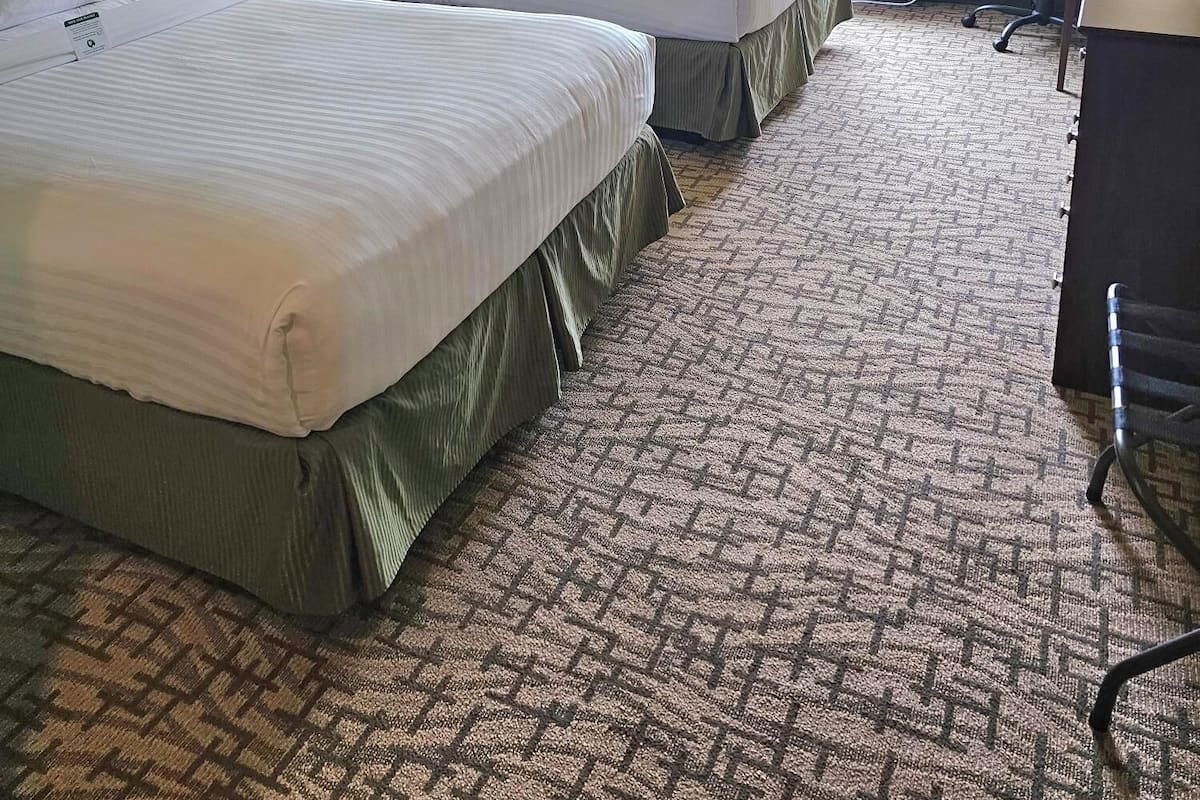 A hotel room with two beds, a desk, and a chair. There are lamps on the nightstands and a window with curtains.
